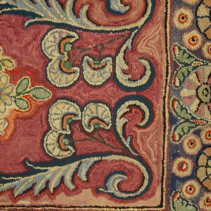 Close-up of a burgundy field with stylized floral motifs in blue and cream, part of the Antique Hooked Rug by Rugs On Net. by Rugs On Net