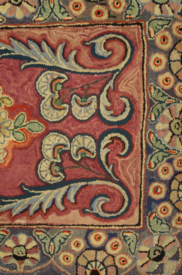 Close-up of a burgundy field with stylized floral motifs in blue and cream, part of the antique hooked rug by rugs on net. By rugs on net