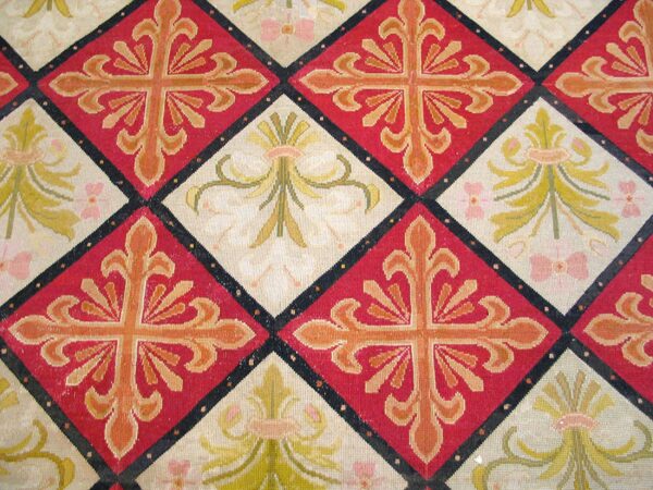 Close-up of a tapestry rug featuring repeating diamond patterns in red and cream with stylized crosses and floral motifs, by rugs on net. By rugs on net