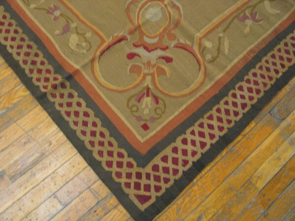 Close-up of a corner of a tapestry rug featuring beige, orange, and dark borders with a repeating geometric pattern by rugs on net. By rugs on net