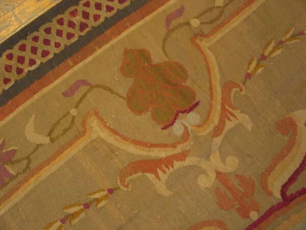 Close-up of a woven textile with tan and gold field colors and stylized floral elements in orange and brown, featuring a geometric border detail, by rugs on net
