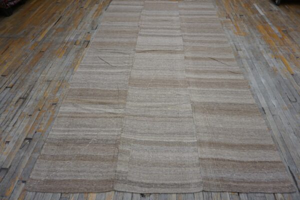 A flatweave rug with horizontal brown and beige stripes, laid on a distressed wooden floor, by rugs on net