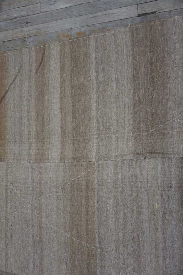 Close-up texture of a neutral beige flatweave rug with vertical striping, showing hand-stitched details against a weathered wood floor, by rugs on net