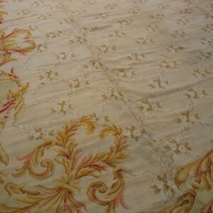 Close-up texture of a beige rug with faint floral pattern and gold/pink scrolling border design by Rugs On Net