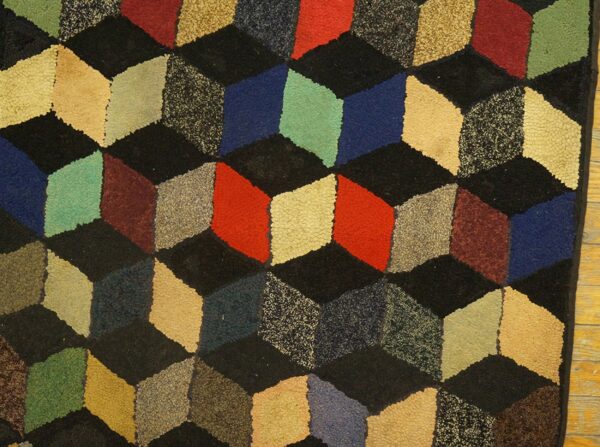 A textured, close-up view of the geometric cube illusion rug featuring a repeating pattern of multicolored, three-dimensional cubes in shades of red, blue, green, and beige on a black background by rugs on net