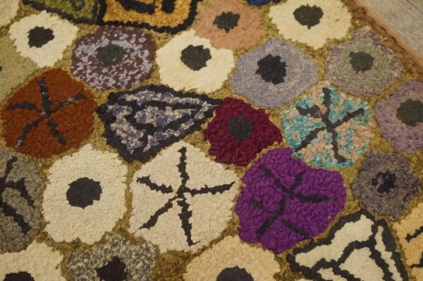 Close-up of a colorful hooked rug with abstract floral shapes in purple, red, cream, and brown by rugs on net. By rugs on net
