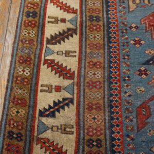 Close-up of a vibrant tribal rug border with geometric patterns in red, blue, and cream, resting on aged wooden floorboards by Rugs On Net. by Rugs On Net