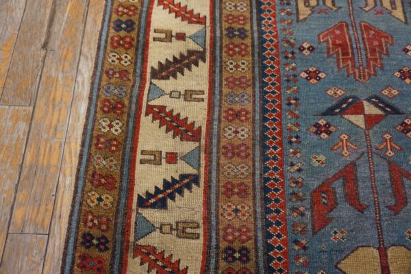 Close-up of a vibrant tribal rug border with geometric patterns in red, blue, and cream, resting on aged wooden floorboards by rugs on net. By rugs on net