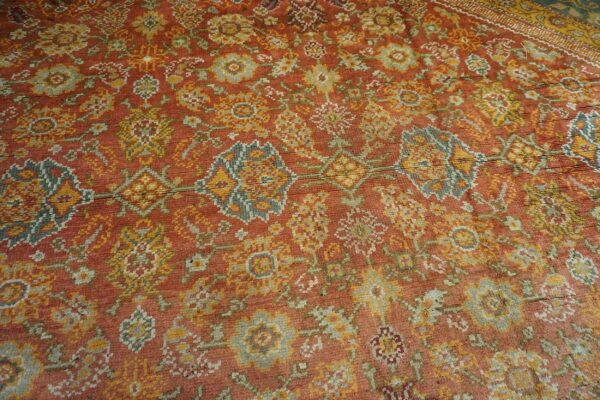 Close-up of a richly colored, distressed rug with terracotta, gold, and muted blue-green floral motifs, by rugs on net. By rugs on net