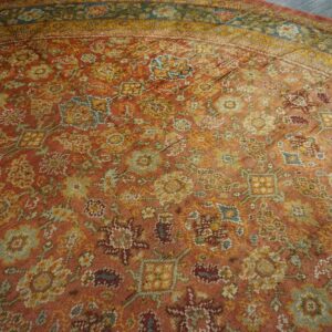 Close-up of a distressed, rust-colored area rug with muted floral and geometric patterns in gold and teal by Rugs On Net. by Rugs On Net