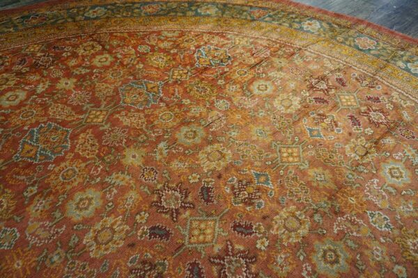 Close-up of a distressed, rust-colored area rug with muted floral and geometric patterns in gold and teal by rugs on net. By rugs on net