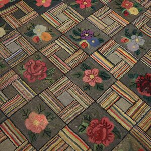 Close-up of a hooked rug featuring a repeating block pattern with colorful floral motifs on a dark ground, by Rugs On Net