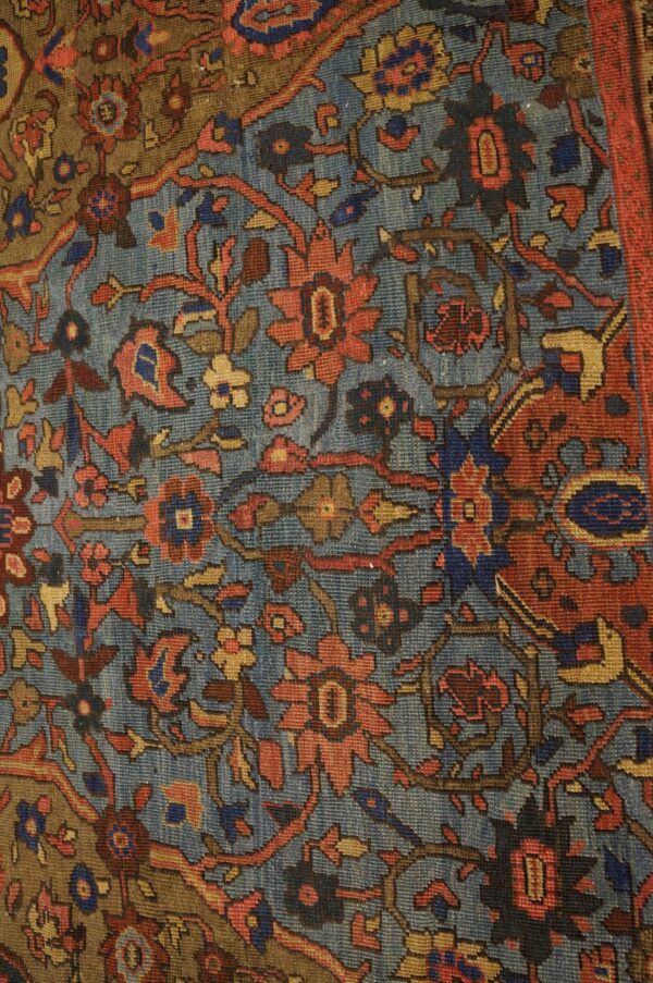 Close-up of an antique rug featuring blue, red, and gold floral motifs on a muted blue ground, by rugs on net. By rugs on net