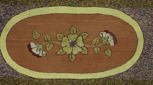 Close-up of an oval floral hooked rug featuring a central yellow flower design on a rust-colored ground, framed by a lime green border by rugs on net