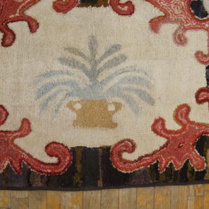 Close-up of a hooked rug featuring a central vase and foliage design framed by red, swirling motifs, by Rugs On Net. by Rugs On Net