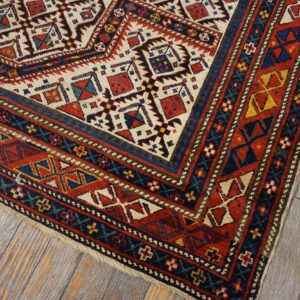 Close-up of a geometric tribal rug corner with red, blue, and cream motifs on distressed wood flooring by Rugs On Net