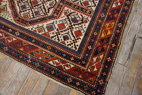Close-up of a geometric tribal rug corner with red, blue, and cream motifs on distressed wood flooring by rugs on net