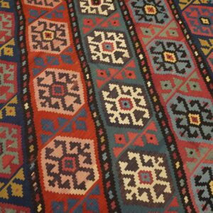Close-up of a vibrant, geometric kilim rug pattern featuring alternating vertical stripes of medallions in red, blue, and teal backgrounds, by Rugs On Net