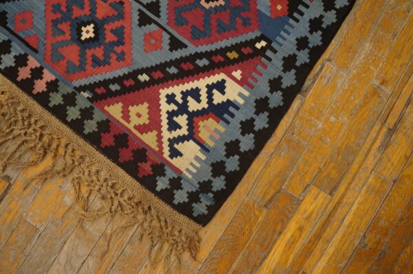 Close-up of a vibrant geometric kilim rug with blue, red, and black patterns, featuring fringed edge on distressed yellow wood floor by rugs on net