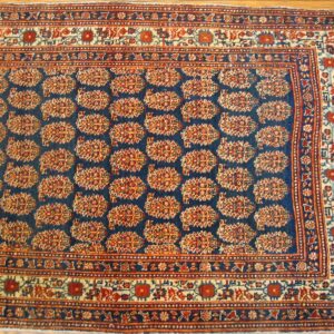 Close-up of a traditional rug with repeating stylized floral motifs on a dark blue field, bordered by geometric patterns in red and cream, by Rugs On Net