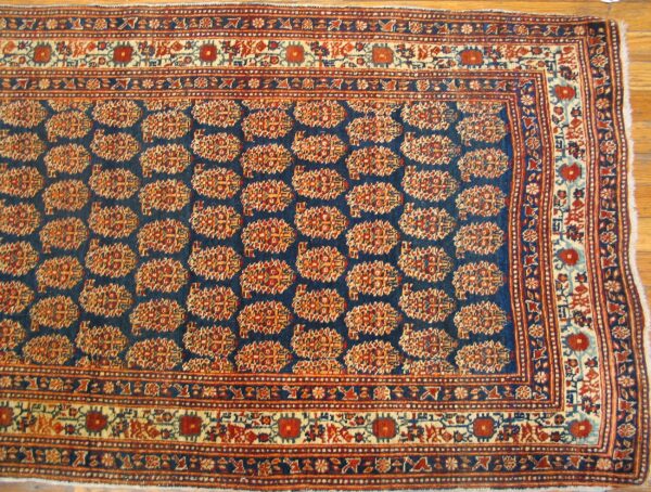 Close-up of a traditional rug with repeating stylized floral motifs on a dark blue field, bordered by geometric patterns in red and cream, by rugs on net