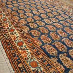 Close-up of a blue field rug with repeating paisley motifs in orange and cream, by Rugs On Net