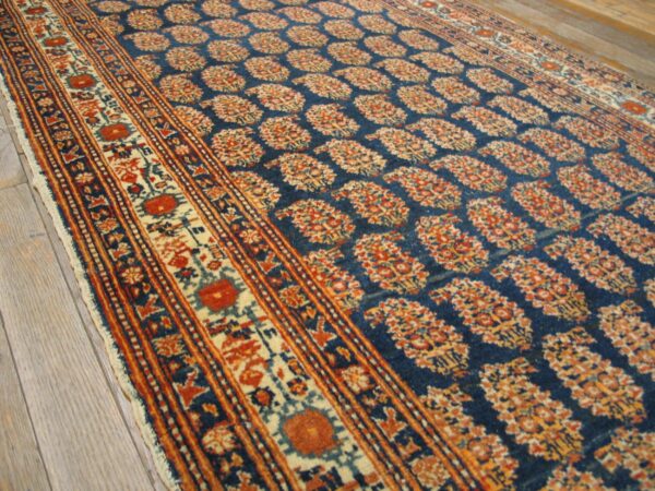 Close-up of a blue field rug with repeating paisley motifs in orange and cream, by rugs on net