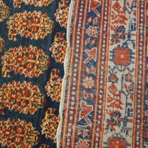 Close-up of a dark blue rug with repeating orange/red motifs next to the reverse side of a patterned rug border by Rugs On Net