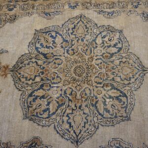 Close-up of a faded, ornate rug featuring a large central medallion with blue and tan floral motifs on a beige ground, by Rugs On Net