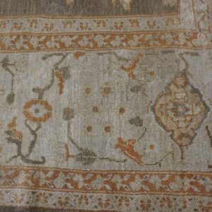 Close-up of a light field rug with faded orange and grey floral motifs and a geometric border by Rugs On Net