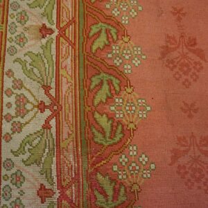 Close-up of the border detail on a salmon-colored rug featuring green and white floral motifs by Rugs On Net. by Rugs On Net