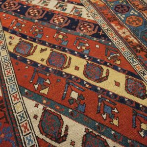 Close-up of a richly colored, antique Caucasian rug with geometric patterns in red, blue, and cream by Rugs On Net. by Rugs On Net