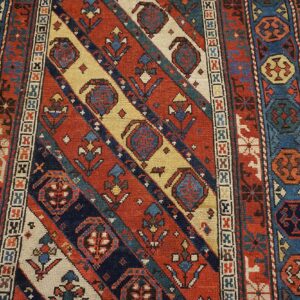 Close-up of a richly colored rug with diagonal stripes and geometric motifs in red, blue, and cream, by Rugs On Net