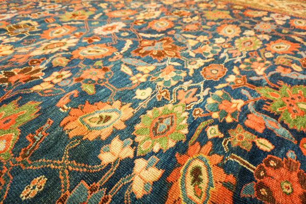 Close-up of a deep blue field with vibrant orange and green floral motifs on the persian rug by rugs on net. By rugs on net