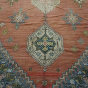 Close-up of a richly textured, salmon-pink rug featuring geometric patterns in faded blues and creams, centered around a diamond medallion, by Rugs On Net. by Rugs On Net