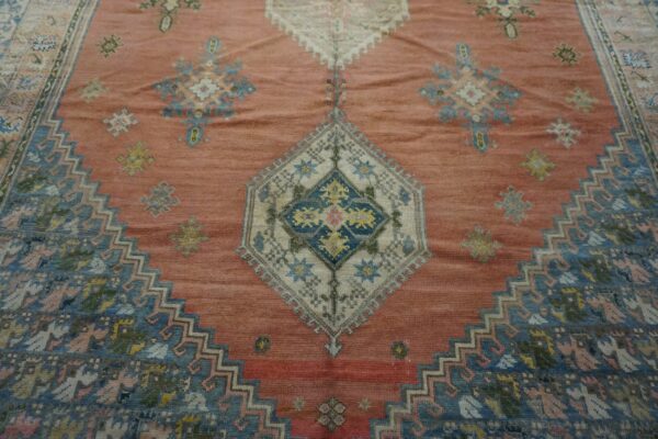 Close-up of a richly textured, salmon-pink rug featuring geometric patterns in faded blues and creams, centered around a diamond medallion, by rugs on net. By rugs on net