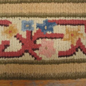 Close-up of a hooked rug border featuring stylized floral motifs in red, blue, and yellow on a cream background, bordered by tan and olive stripes, by Rugs On Net