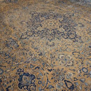 Close-up view of a faded antique Persian rug with gold and navy blue floral patterns by Rugs On Net. by Rugs On Net
