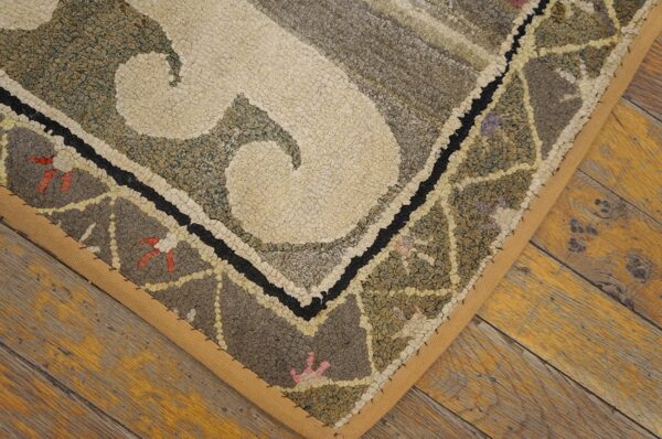Close-up of a hooked rug corner with cream and muted green/grey patterns on a wooden floor by rugs on net. By rugs on net