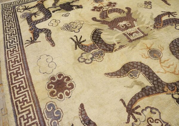 Close-up of a beige rug featuring dark brown and purple dragon motifs and cloud patterns, with a geometric border, by rugs on net