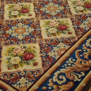 Close-up of a needlepoint rug featuring floral medallions on a cream background framed by a blue border with gold scrolling by Rugs On Net. by Rugs On Net