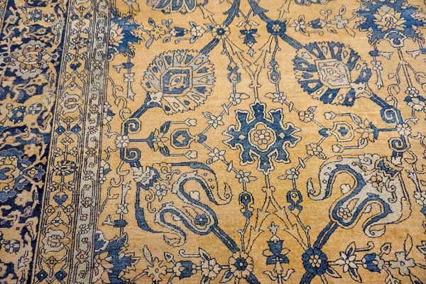 Close-up of the gold field and blue floral motifs of an antique persian rug by rugs on net. By rugs on net