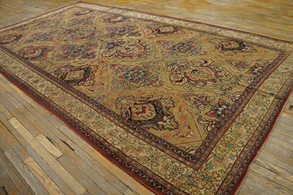 A large, antique persian rug with a repeating geometric pattern in gold, red, and blue tones, displayed on a wooden floor by rugs on net. By rugs on net