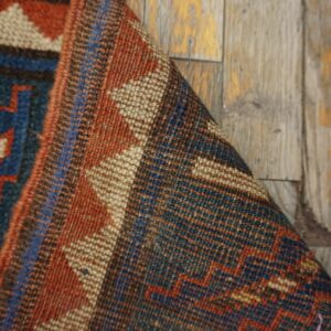 Close-up of a folded tribal rug with geometric patterns in red, blue, and beige on a distressed wooden floor by Rugs On Net