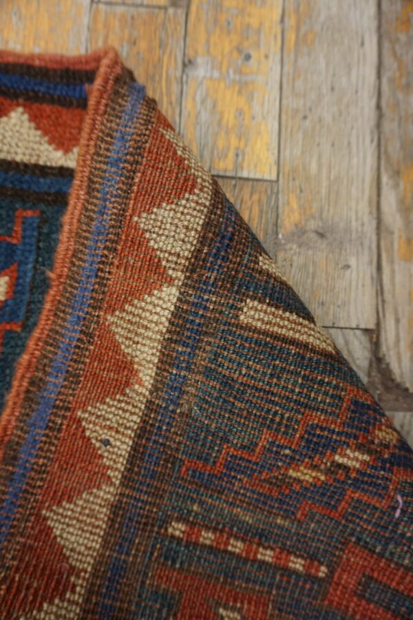 Close-up of a folded tribal rug with geometric patterns in red, blue, and beige on a distressed wooden floor by rugs on net