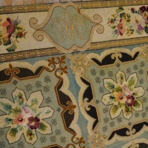 Close-up of a needlepoint rug border featuring floral motifs and a central initial 'W' on a pale blue field, by Rugs On Net. by Rugs On Net
