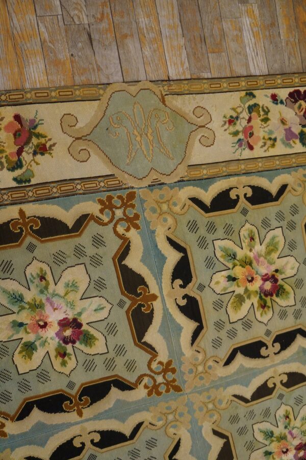 Close-up of a needlepoint rug border featuring floral motifs and a central initial 'w' on a pale blue field, by rugs on net. By rugs on net