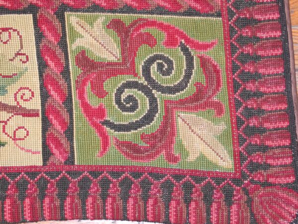 Close-up of a needlepoint rug border featuring red, green, and black geometric patterns and tassels, by rugs on net. By rugs on net