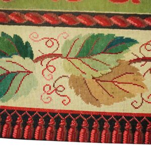 Close-up of a needlepoint rug border featuring green and brown grape leaves with red vines against a cream background, finished with red tassels by Rugs On Net. by Rugs On Net