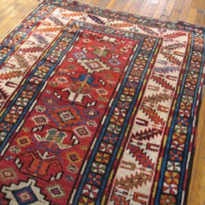 Close-up of a vibrant, antique Caucasian rug with geometric patterns on a wooden floor by Rugs On Net